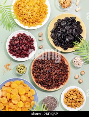 Trockene Früchte, Nüsse und Samen auf blauem Hintergrund mit Palmblättern. Gesunder Snack - Mischung aus Bio-Nüssen und trockenen Früchten. Vegan und vegetarisch Stockfoto