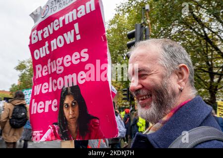 Ein lächelnder Mann trägt ein Plakat „Braverman jetzt raus! Flüchtlinge sind hier willkommen“, während einer Demonstration gegen die konservative Regierung. Stockfoto