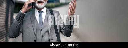 Mittelteil glücklicher professioneller Gespräche auf dem Smartphone. Lächelnder Geschäftsmann mit einer Tasche, während er gegen das Bürogebäude steht. Er trägt Stockfoto