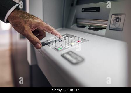 Zugeschnittenes Bild eines Geschäftsmanns, der eine PIN in einen Geldautomaten eingibt. Nahaufnahme eines älteren männlichen Berufs zieht Geld ab. Er nutzt Electronic Banking. Stockfoto