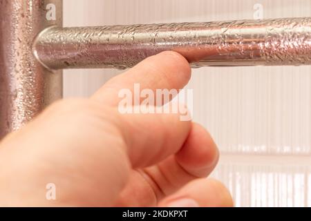 Die Hand berührt das Kondensat auf dem beheizten Handtuchhalter. Nahaufnahme Stockfoto