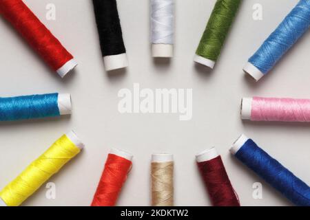 Mehrfarbige Fäden in Spulen, in einem Kreis auf grauem Hintergrund angelegt. Stockfoto