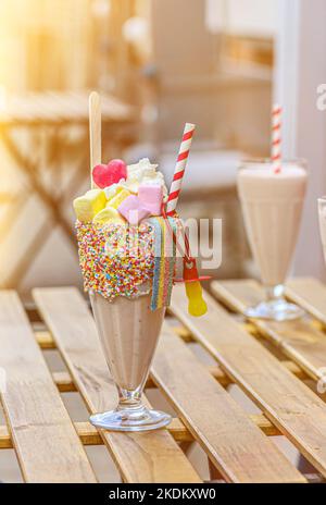 Zwei Freak-Shakes mit Marschwalbe, Baiser und Marmelade auf einem Holztisch in einem Café. Stockfoto