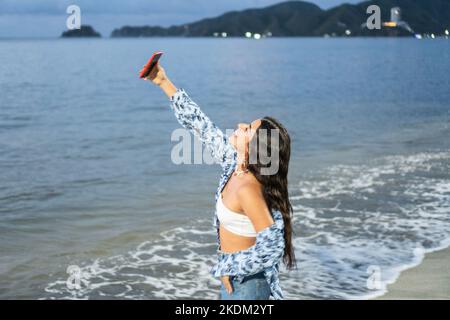 Hispanische Frau Lacht Beim Selfie Mit Handy Am Strand Stockfoto