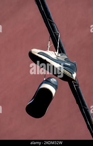 Barcelona, Spanien - 24. Oktober 2022: Schuhe hängen an einem Kabel, das die Straße eines Viertels überquert, gemeinsamer Streich in Vorstadtvierteln