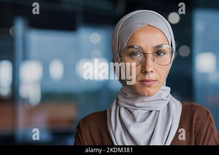 Nahaufnahme Porträt einer erfolgreichen denkenden Geschäftsfrau mit Hijab und Brille, Frau mit Blick auf die Kamera, die im modernen Bürogebäude arbeitet. Stockfoto