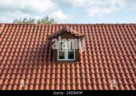 Rotes Ziegeldach mit Dachboden. Dachfenster weiß auf Dachboden. Wolkiger Himmel im Hintergrund. Stockfoto