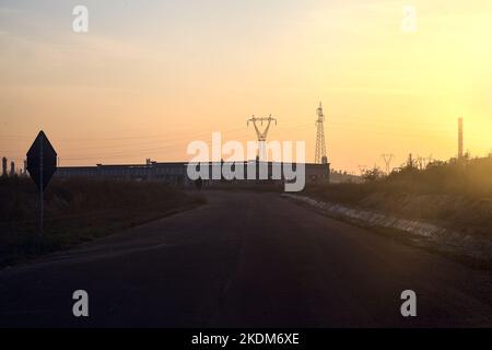 Leere Straße mit verlassenen Lagerhäusern und Pylonen bei Sonnenuntergang Stockfoto