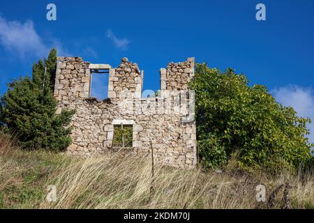 Zerstörte Fassade eines verlassenen Gebäudes, beschädigte Steinmauer Haus in ländlicher Umgebung, Trockenanlage, Baum, sonnigen Tag blauen Himmel Peloponnes Griechenland. Stockfoto