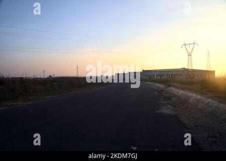 Leere Straße mit verlassenen Lagerhäusern und Pylonen bei Sonnenuntergang Stockfoto