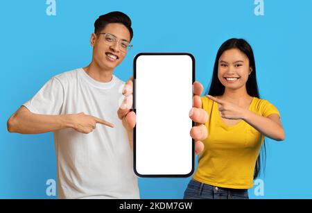 Schönes Angebot. Junge asiatische Paar hält und zeigt auf große leere Smartphone Stockfoto
