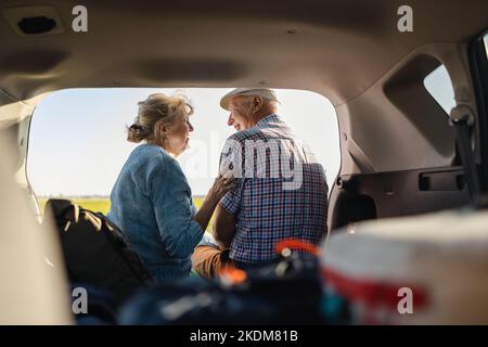 Glückliches Seniorenpaar, das in freier Wildbahn im offenen Kofferraum sitzt Stockfoto