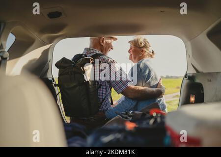 Glückliches Seniorenpaar, das in freier Wildbahn im offenen Kofferraum sitzt Stockfoto