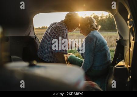 Glückliches Seniorenpaar, das in freier Wildbahn im offenen Kofferraum sitzt Stockfoto