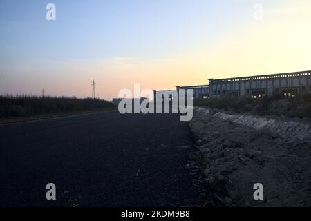 Leere Straße mit verlassenen Lagerhäusern und Pylonen bei Sonnenuntergang Stockfoto