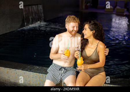 Schönes junges Paar, das sich entspannt und frischen Orangensaft am Pool trinkt Stockfoto