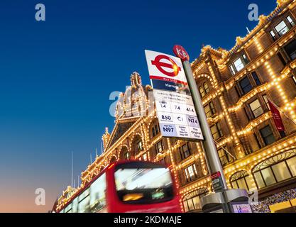 Harrods Kaufhaus mit eigener Bushaltestelle an der Brompton Road bei Sonnenuntergang in der Abenddämmerung, vorbei an verwackelt roten Londoner Bus Wintersaison Knightsbridge London UK Stockfoto
