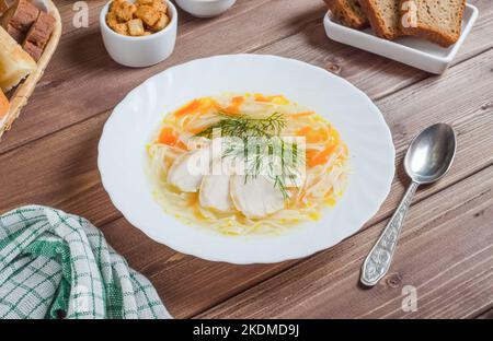 Appetitliche Hühnersuppe mit Nudeln und Fleischstücken auf einem weißen Teller auf dunklem Holzboden, Chefkoch serviert. Stockfoto