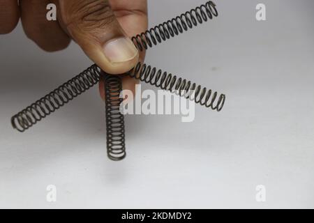 Hand hält vier Druckfedern aus Metall, die an verschiedenen mechanischen Bewegungsmaschinen verwendet werden Stockfoto