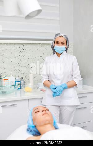 Kosmetikerin in blauer Maske und Frau auf der Couch Stockfoto