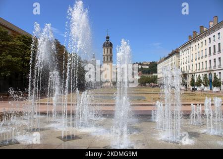 Ein moderner Brunnen mit Blick auf den ehemaligen Glockenturm der Charité-Klinik am Place Bellecour in Lyon, Frankreich. Stockfoto