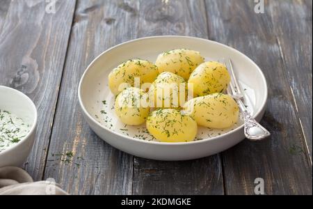 Junge gekochte Kartoffeln mit Dill und Knoblauch-Sour-Cream-Sauce auf einem Holztisch Stockfoto