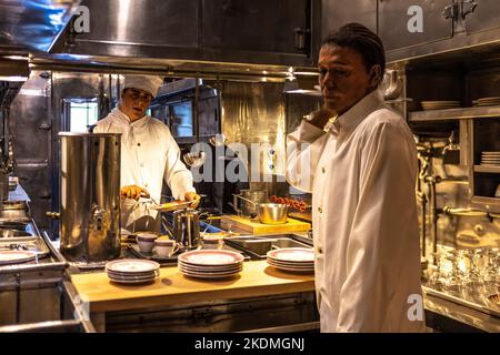 Küchenchef Relica in der Küche eines Speisewagens, der dem Kellner Essen auf den Teller gab Stockfoto