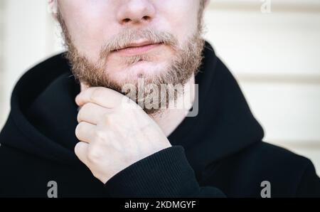 In Nahaufnahme berührt ein junger Mann seinen Bart mit der Hand. Stockfoto