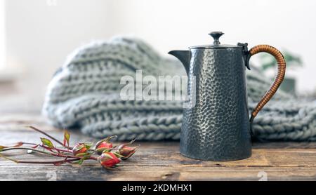 Strukturierte graue Teekane und gestricktes Element auf unscharfem Hintergrund. Stockfoto