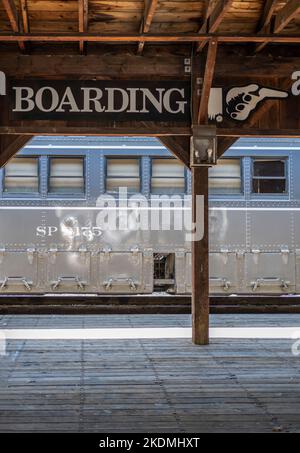 Hölzerner Bahnsteig mit großem Boarding-Schild mit Schild, das die Passagiere in die Richtung weist, in die sie gehen müssen, um in den Zug zu steigen Stockfoto