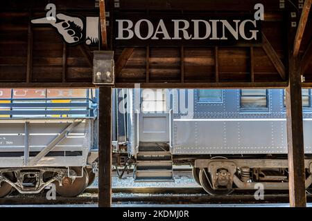 Hölzerner Bahnsteig mit großem Boarding-Schild mit Schild, das die Passagiere in die Richtung weist, in die sie gehen müssen, um in den Zug zu steigen Stockfoto