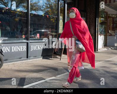 Eine muslimische Frau mittleren Alters, die helle Kleidung trägt, geht auf der Straße 74. in Jackson Heights, Queens, New York City. Stockfoto