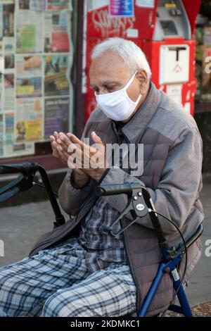 Ein älterer Muslim betet auf dem Diversity Plaza, während er auf seinem Spaziergänger sitzt. In Jackson Heights, Queens, New York City. Stockfoto