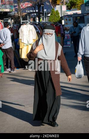 Eine bescheiden gekleidete muslimische Frau mit ihrem Gesicht geht auf dem Diversity Plaza in Queens, New York City. Stockfoto