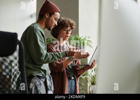 Zwei junge interkulturelle Programmierer diskutieren Online-Daten und äußern sich zum Thema Video, das die Softwareentwicklung beschreibt Stockfoto