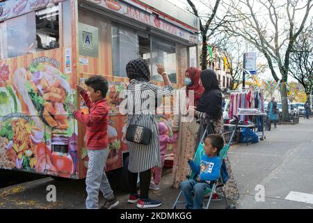 Muslimische Frauen in Hijabs und ihre Kinder kaufen in einem Halal-Lastwagen Lebensmittel ein. In Jackson Heights, Queens, New York City. Stockfoto