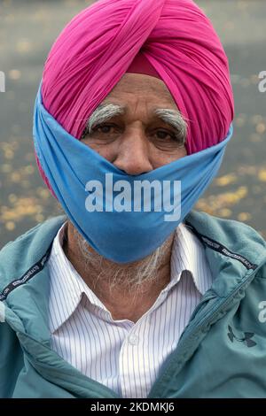 Posierte Porträt eines älteren Sikh-Mannes in einem rosa Turban und Teilmaske. An der 74. Street in Jackson Heights, Queens, New York City. Stockfoto