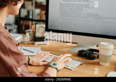 Hände junger weiblicher Programmierer, die auf der Computertastatur tippen, während sie Daten am Arbeitsplatz im Büro auf dem Computerbildschirm entschlüsseln Stockfoto