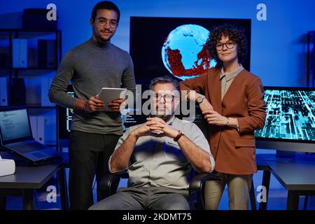 Eine Gruppe von drei erfolgreichen interkulturellen Programmierern, die die Kamera betrachten, während zwei junge Kollegen einen reifen IT-Ingenieur umzingelten Stockfoto
