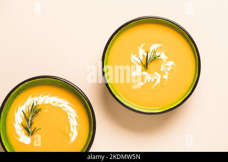 Zwei grüne Schalen mit dickem Butternut-Squash-Bisque, garniert mit schwerer Creme und Rosmarin auf hellem Hintergrund. Schüssel mit Kürbis und Karotte Creme sou Stockfoto