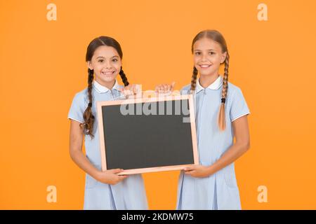 Fröhliche Freunde in Retro-Uniform. Vintage-Kid-Mode. Zurück zur Schule. Kleine Mädchen halten Tafel. Kindererziehung. Mädchen präsentieren Informationen Stockfoto