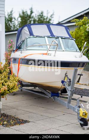 Kleines Motorboot auf Anhänger in der Auffahrt in der Nähe des Hauses geparkt. Stockfoto