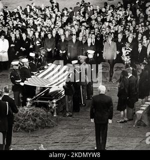 Foto von Soldaten, die die Flagge aus der Schatulle von Präsident John F. Kennedy auf dem Nationalfriedhof von Arlington entfernen, während die Witwe des verstorbenen Präsidenten und andere Trauernde darauf blicken - 25. November 1963 Stockfoto