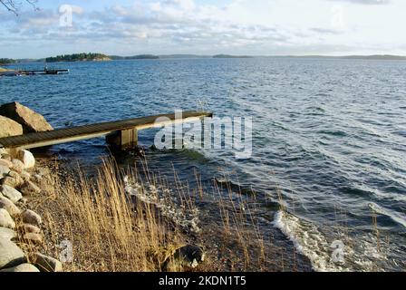 Küstenlinie mit einem hölzernen Steg im Wasser und Schilfpflanzen im Vordergrund. Stockfoto