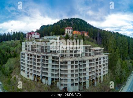 Das mehrstöckige verlassene Hotel mit Betonwänden liegt in einem dichten Fichtenwald am Hang des Hochtals der Rhodopen-Berge. Panorama, Draufsicht Stockfoto