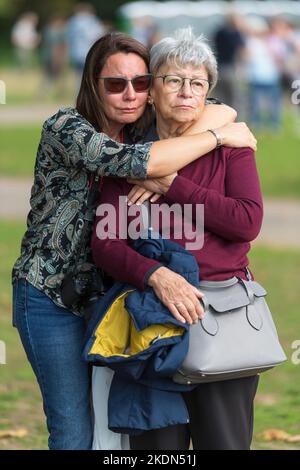 Zwei Frauen umarmen sich, während sie die Live-Übertragung des Sarges Ihrer Majestät der Königin beobachten, der von einem Militärzug vom Buckingham Palace zum gebracht wird Stockfoto