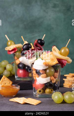 Jarcuterie in zwei Glas umfasst verschiedene Arten von Wurst, Gurken, Käse, Nüsse, Gemüse und Obst. Moderne Version von festlichen Snack auf grünen Bac Stockfoto