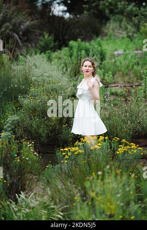 Frau in einem kurzen weißen Kleid auf einem Gartenpfad stehend Stockfoto