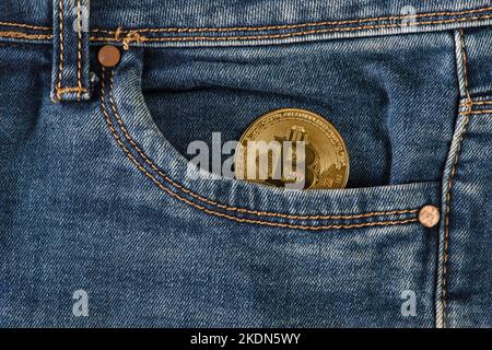 Bitcoin in der Tasche. In der Tasche der blauen Jeans liegt eine goldene Bitcoin-Münze. Gehalt in Bitcoins, Einkommen in Kryptowährung. Stockfoto