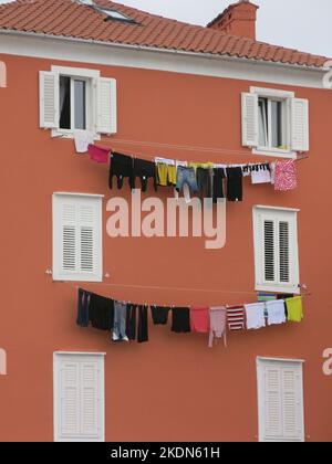 Die Wäscheseile hängen zwischen den Fenstern dieses bunten Gebäudes in der alten kroatischen Stadt Cres zum Trocknen an Kabeln. Stockfoto